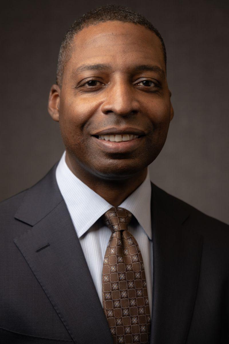 Mr. 詹姆斯·凯西, an African American Male wearing a grey suit jacket with a white collared shirt and a red tie with gold dots.