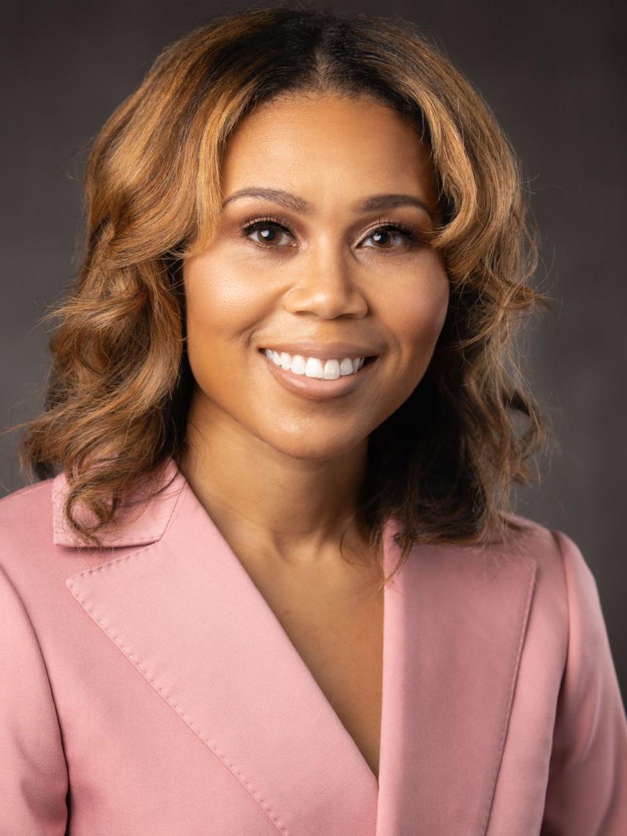 Ms. Katrell纳什, an African American female with long caramel colored hair, smiles wearing a pink suit jacket on a grey background.