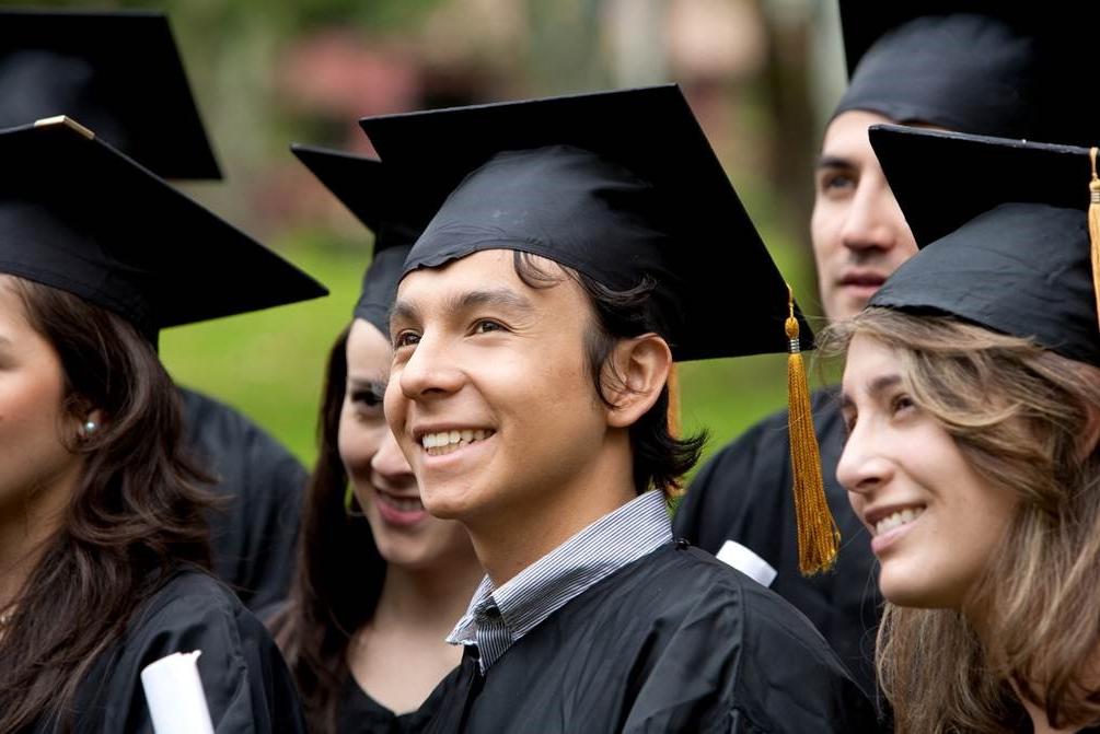 森林的绿色, 超链接, button labeled 准度 in white, 粗体, underlined text with an image of six graduates smile to the right of the frame in black graduate caps and gowns: A Caucasian female with sandy, brown hair stands to the right of a smiling, 棕色的头发, Caucasian male with a blue collared shirt showing above his gown. 他的左边是一个棕色头发的人, Caucasian female stands smiling with another 棕色的头发, Caucasian female standing partially out of the frame to her left. A Caucasian male stands partially blocked by the first female and a sixth graduate stands hidden behind the last female.